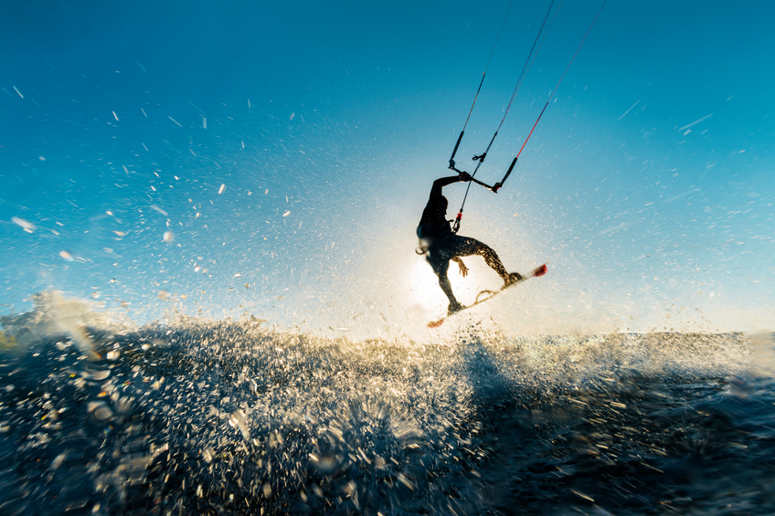 Image of a surfer doing an amazing jump and splashing water in front of the sunset at the sea