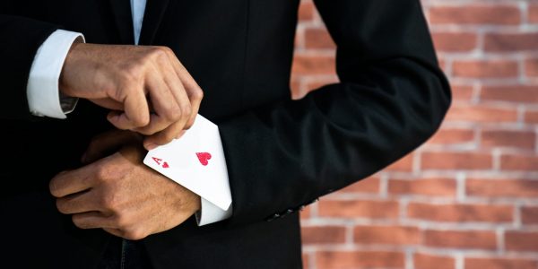 Abstraktes Bild eines Geschäftsmann der ein Pik Ass aus dem Ärmel zabuert als Metapher für "Open banking poker—Winner takes all"